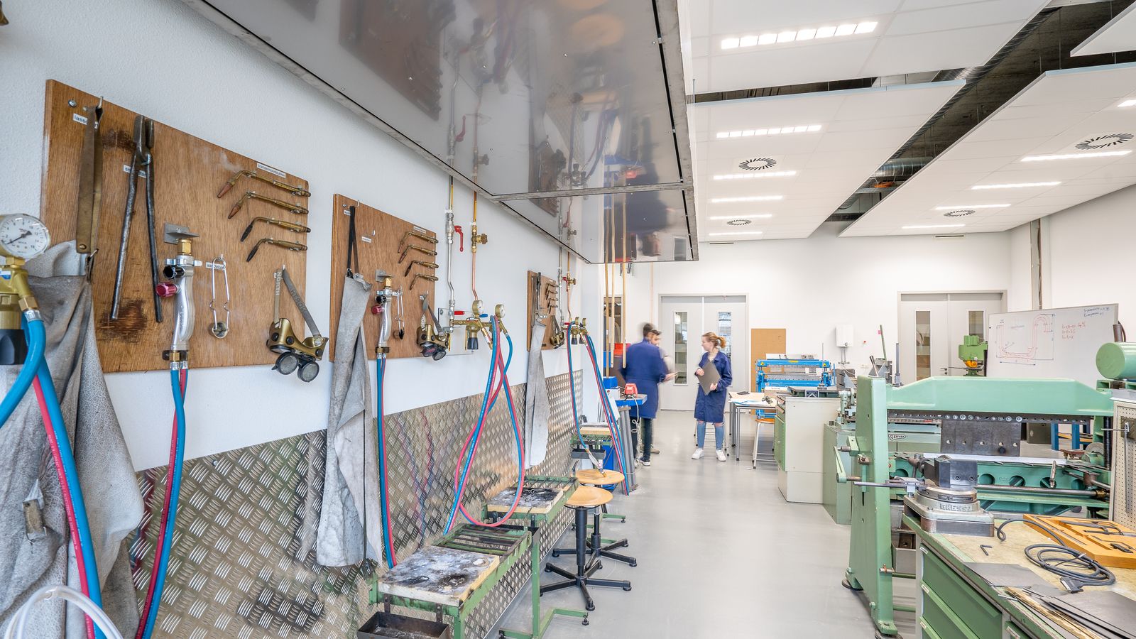 Bright, wide shop aisle lined with workbenches, tool boards, and machines